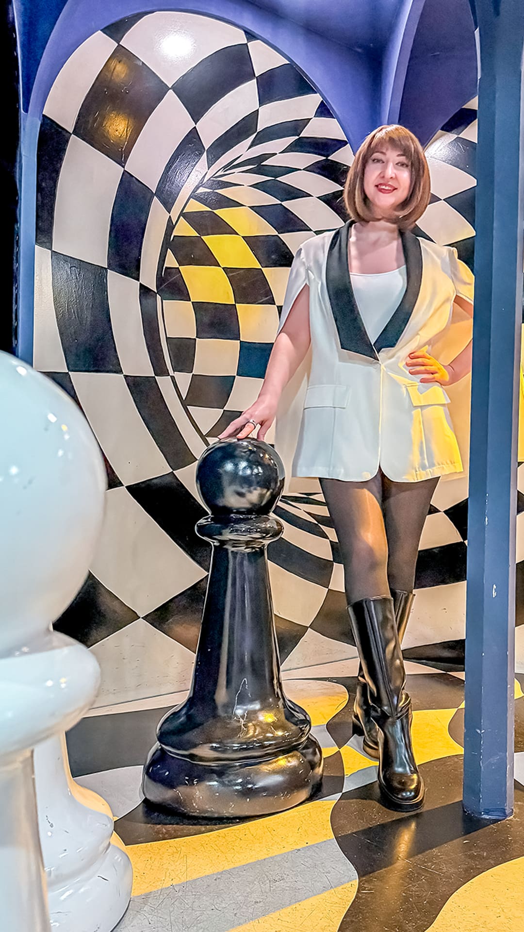 Visitor posing between two giant black chess pawns against a spiralling black-and-white optical-illusion wall at Alice in Wonderland Barcelona